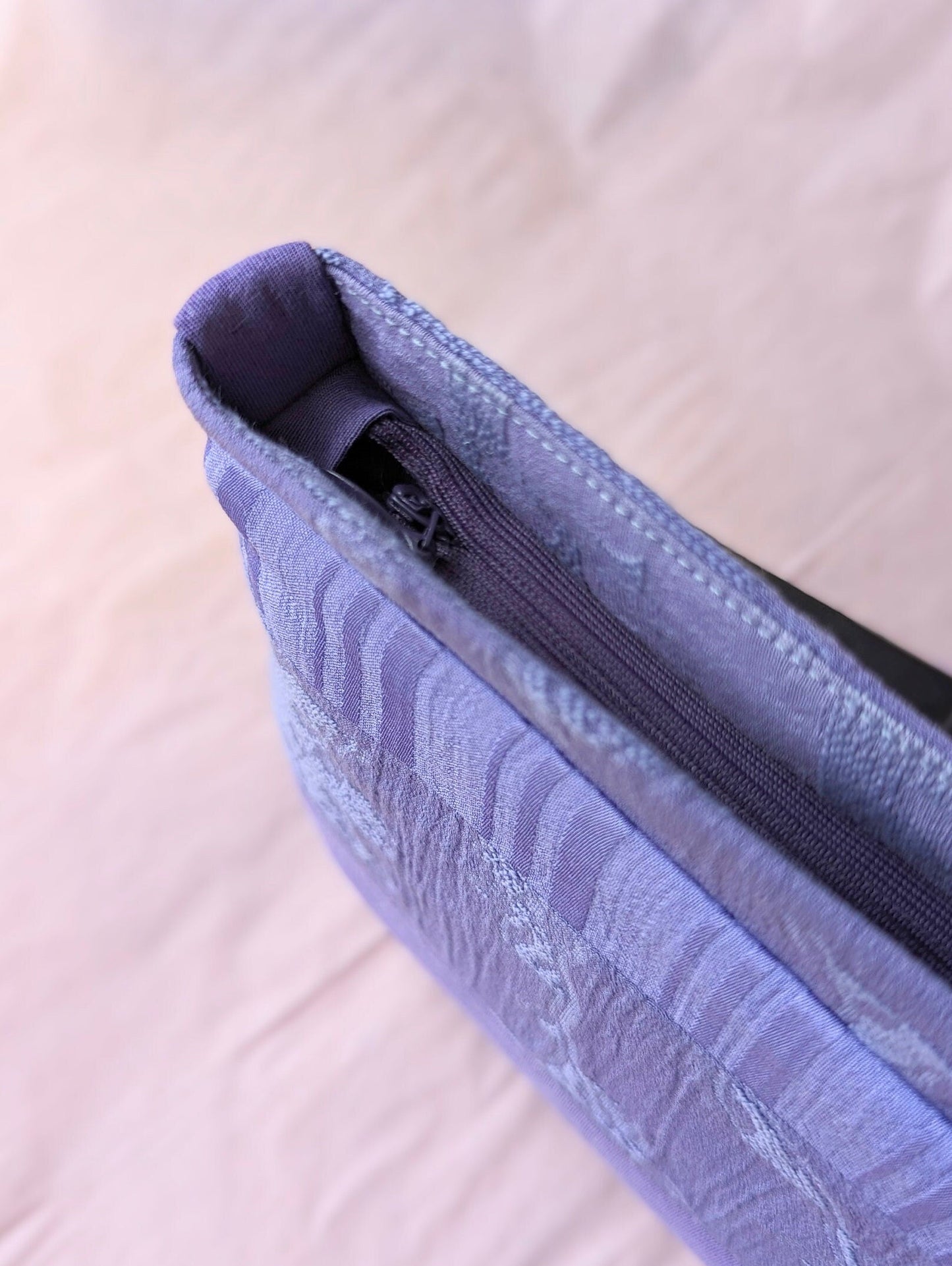This photo is taken from above the purse. It shows the zipper which is also purple, the same as the bag. There is a fabric tab which folds over the lip of the opening which squares off the opening