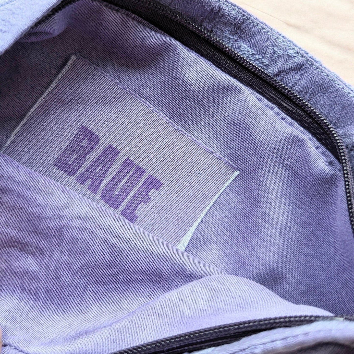 Close up image of the brand label. It is attached to the lining of the makeup bag, on the inside. The label reads B A U E which is pronounced bower. The label is made from a rectangle of the silk fabric you can see on the outside of the makeup bag