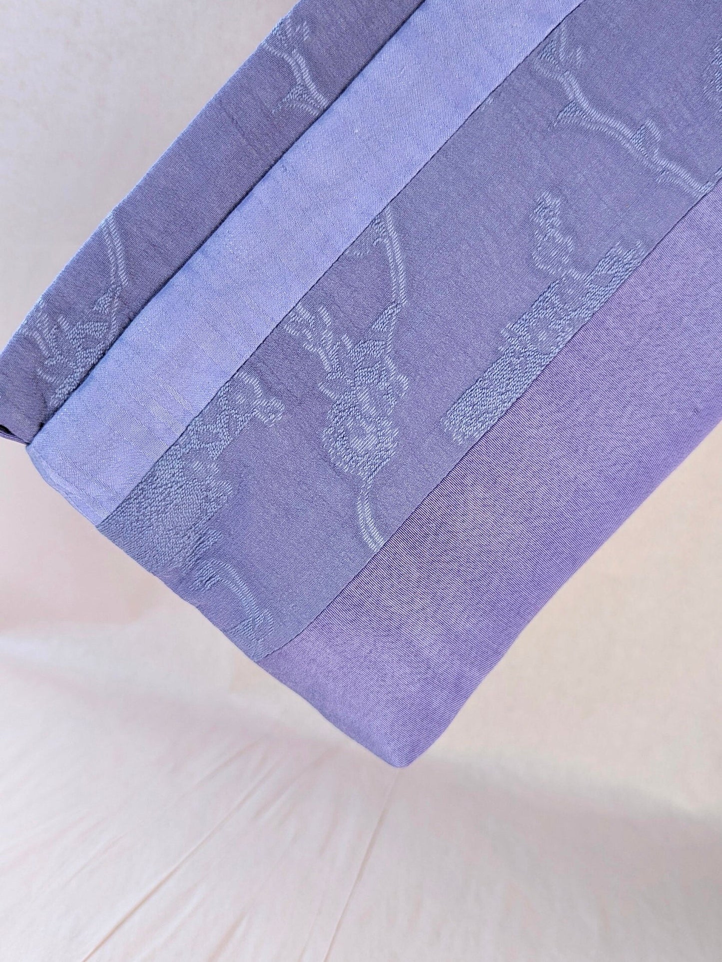 Here the makeup pouch is held diagonally close to the camera. It is a light, bright lavender colour. It is made of fabrics patchworked together to create different width stripes.