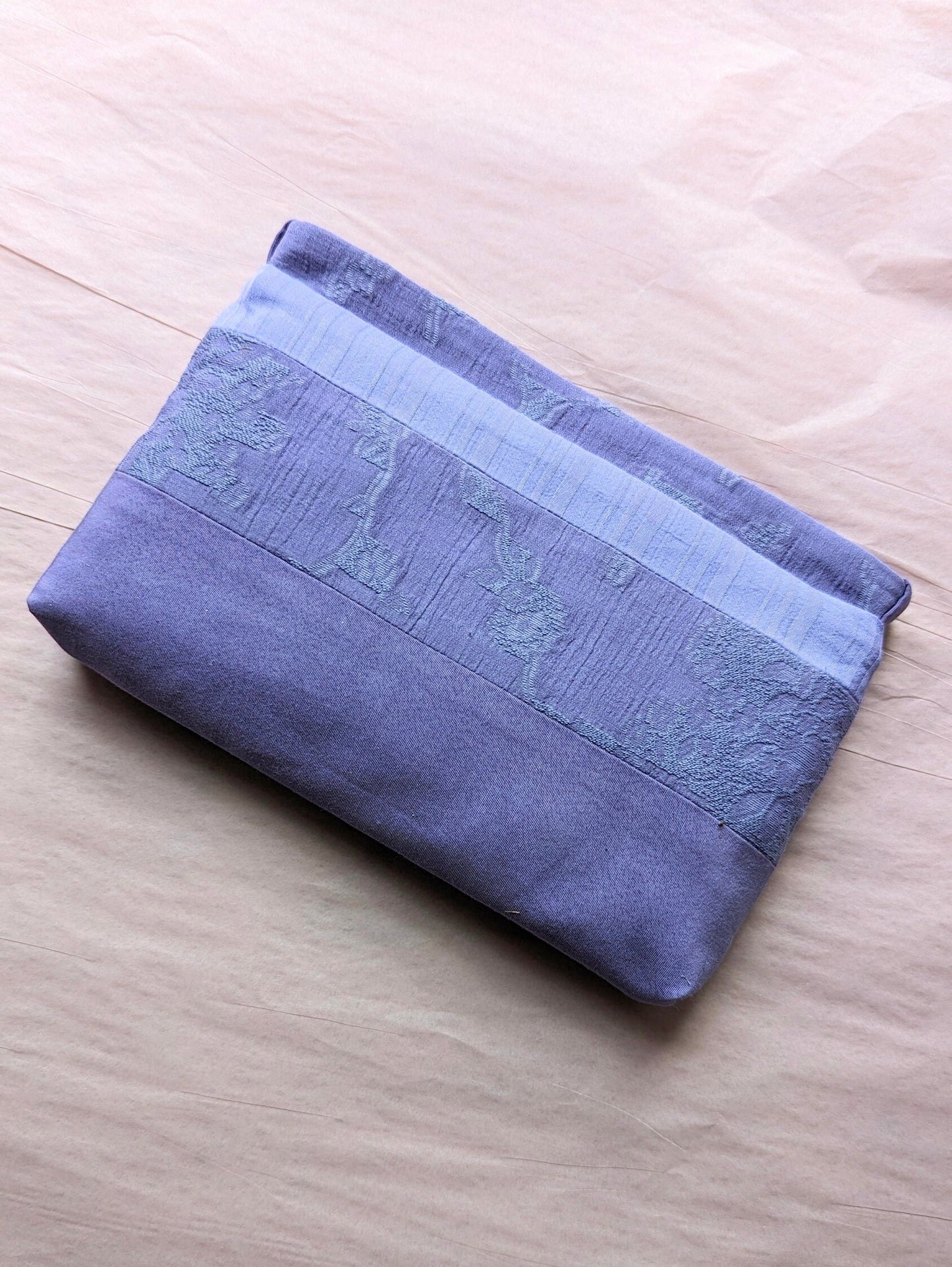 This image shows the makeup bag lieing flat on very pale pink tissue paper. You can see that one of the fabric stripes has a subtle floral texture and another section has a stripe texture.