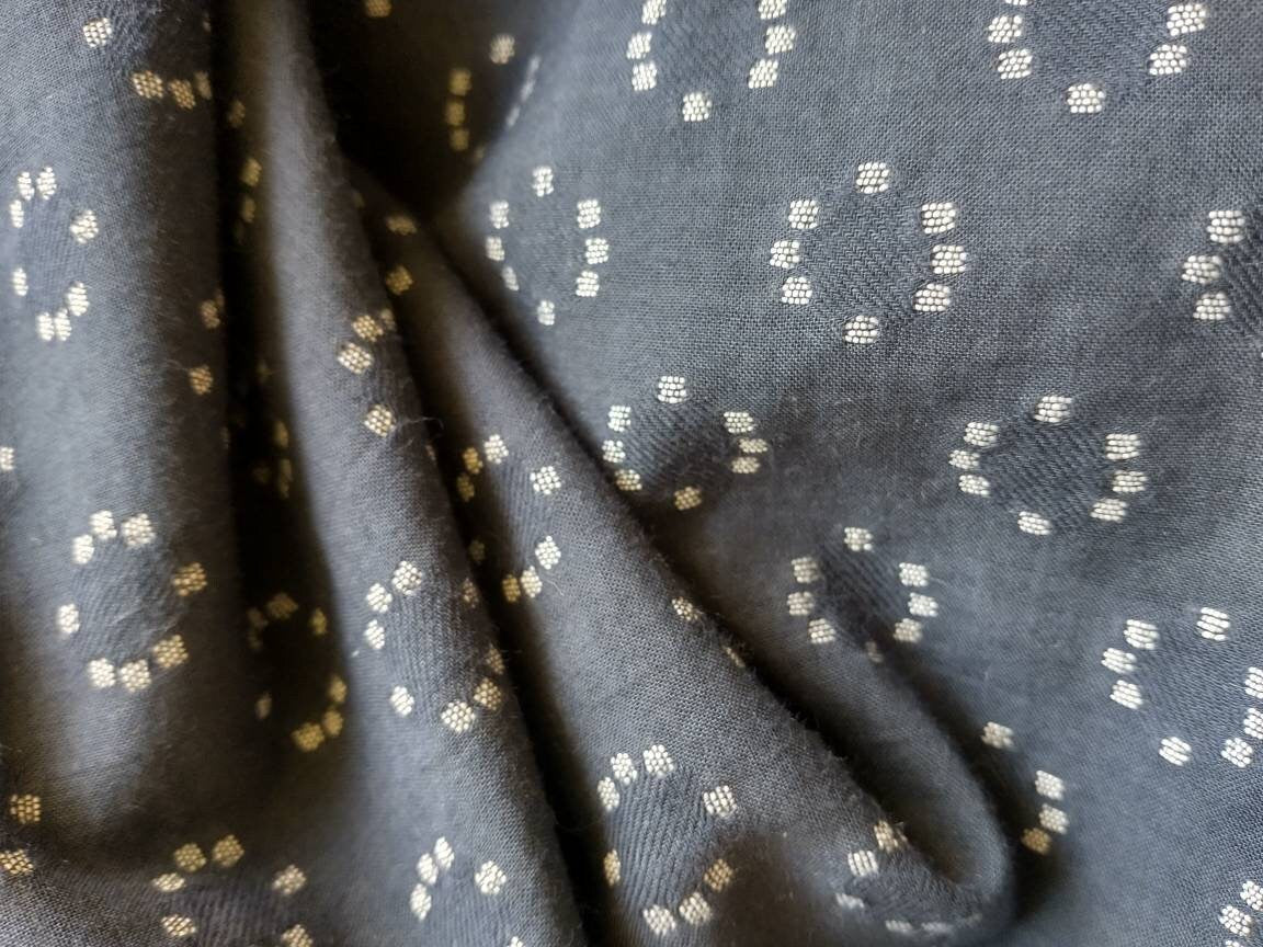 The dusky blue cotton fabric has a pattern woven into it in off-white thread. The pattern is small circles made up of 8 tiny dots repeated over all the fabric. The fabric is soft and drapey.
