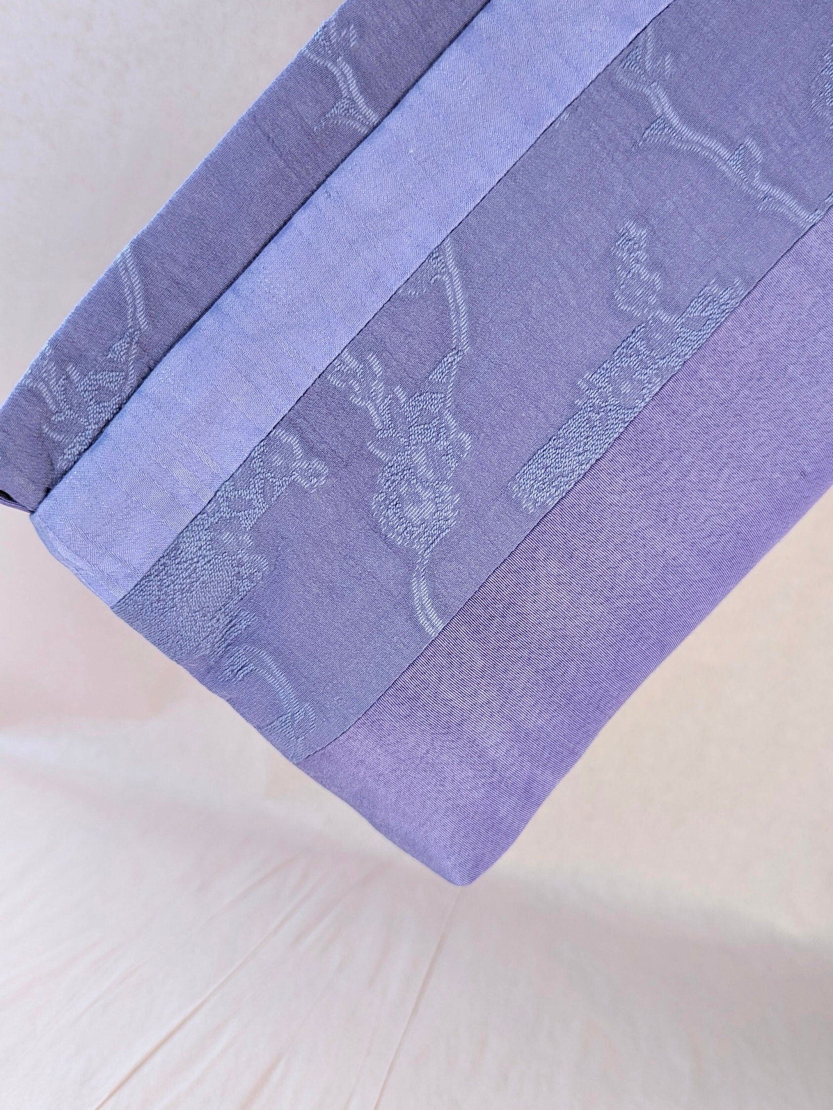 Here the makeup pouch is held diagonally close to the camera. It is a light, bright lavender colour. It is made of fabrics patchworked together to create different width stripes.